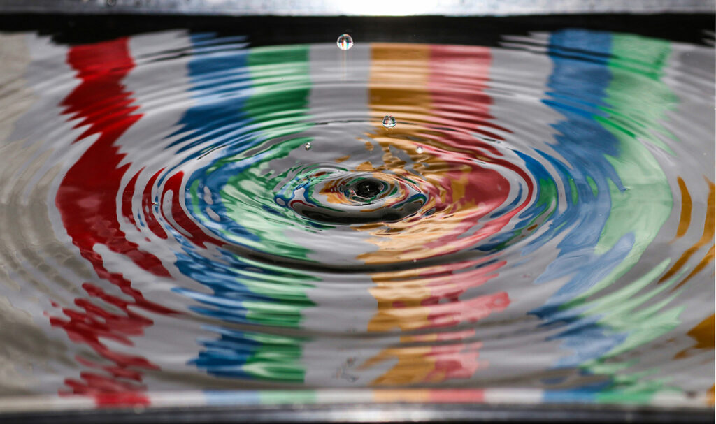 Photograph of the impact of a drop of water creating large colourful ripples across a surface