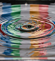 Photograph of the impact of a drop of water creating large colourful ripples across a surface